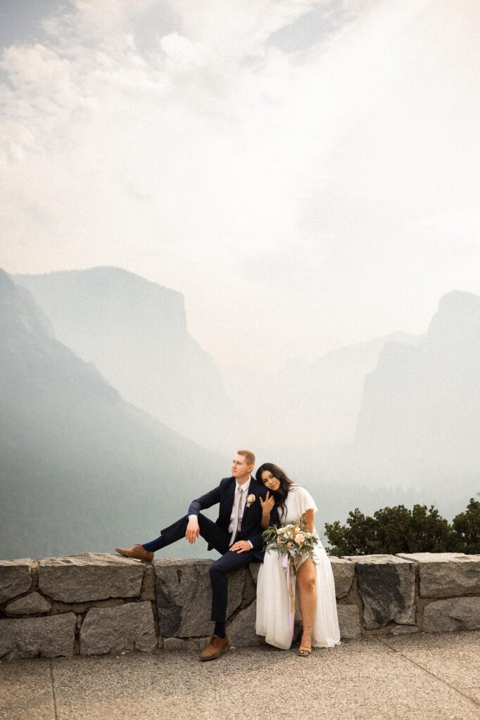 Couple sitting on the ledge at Tunnel View watching sunset during the best time to elope in Yosemite